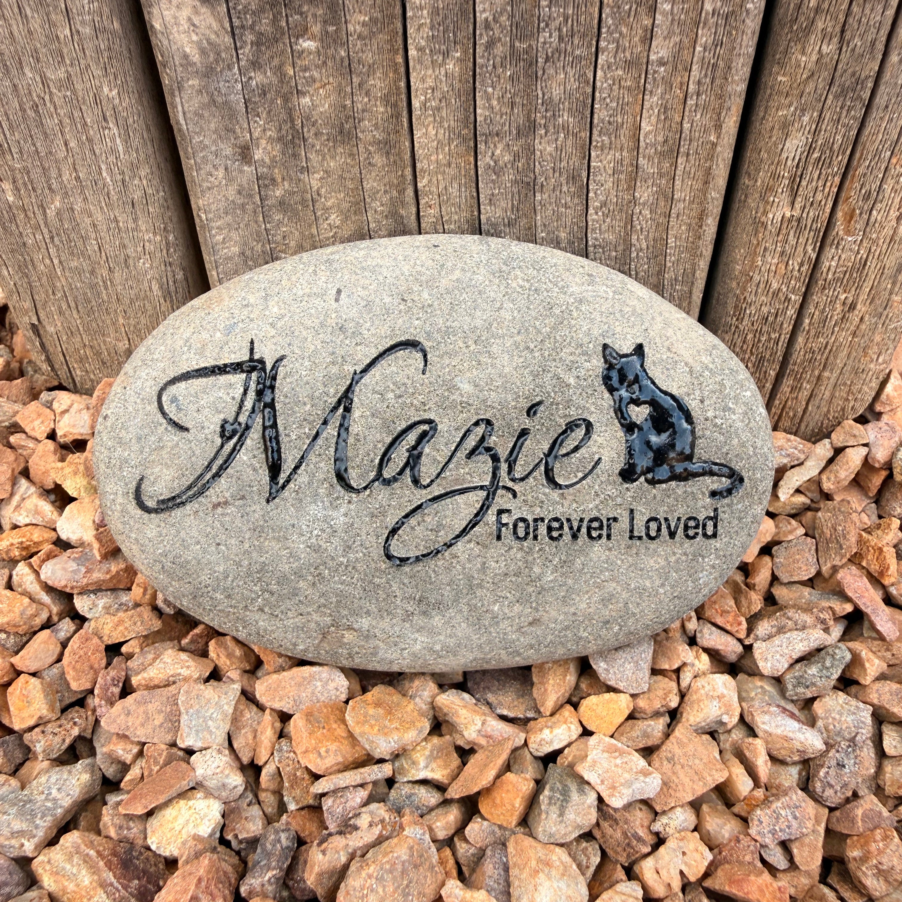 Decorative stone with engraved text on a wooden surface and gravel background