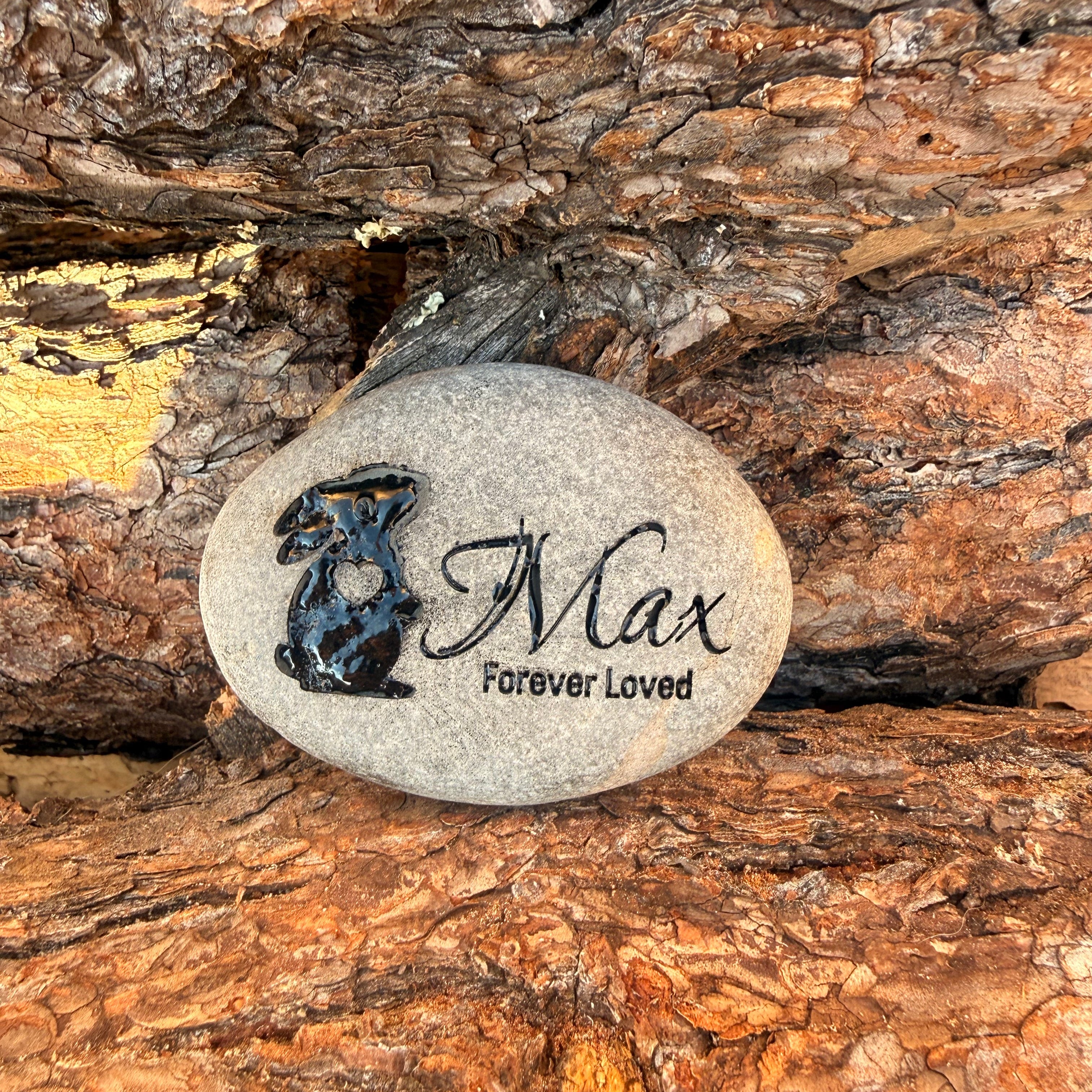Decorative memorial stone sitting against tree bark. Stone has an engraving of a rabbit with a heart, the pet's name and the statement "Forever Loved". 